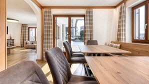 Een eetruimte met een houten tafel en lederen stoelen, grote ramen met gordijnen en uitzicht op de omgeving.
