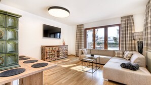 Een moderne woonkamer met een houten eettafel, een bank en een aan de muur bevestigde televisie.