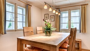 A dining area with a wooden table, chairs, a vase with flowers, and large windows with curtains. - Chalet Mariedl in Tschagguns (Tschagguns)