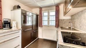 A modern kitchen with stainless steel appliances, a built-in oven, a coffee maker, and a window with curtains. - Chalet Mariedl in Tschagguns (Tschagguns)