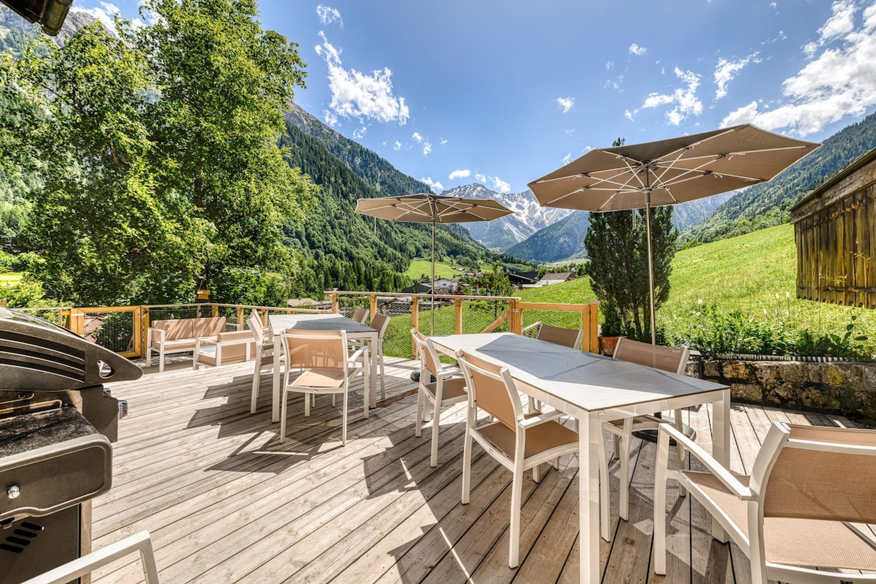 Una terrazza in legno con posti a sedere all'aperto, un barbecue e vista sulle montagne.
