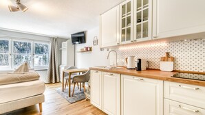 Une cuisine moderne avec des meubles blancs, un plan de travail en bois et une fenêtre donnant sur les arbres.