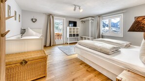 Une chambre à coucher avec un lit, une commode, un téléviseur et une vue sur les montagnes par la fenêtre.