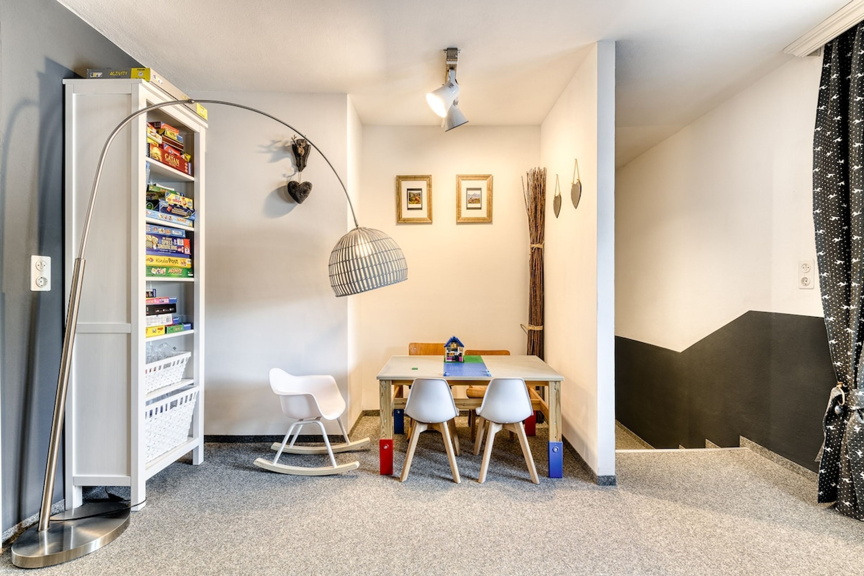 A room with a white bookshelf, a table with two chairs, a rocking chair, and a floor lamp.