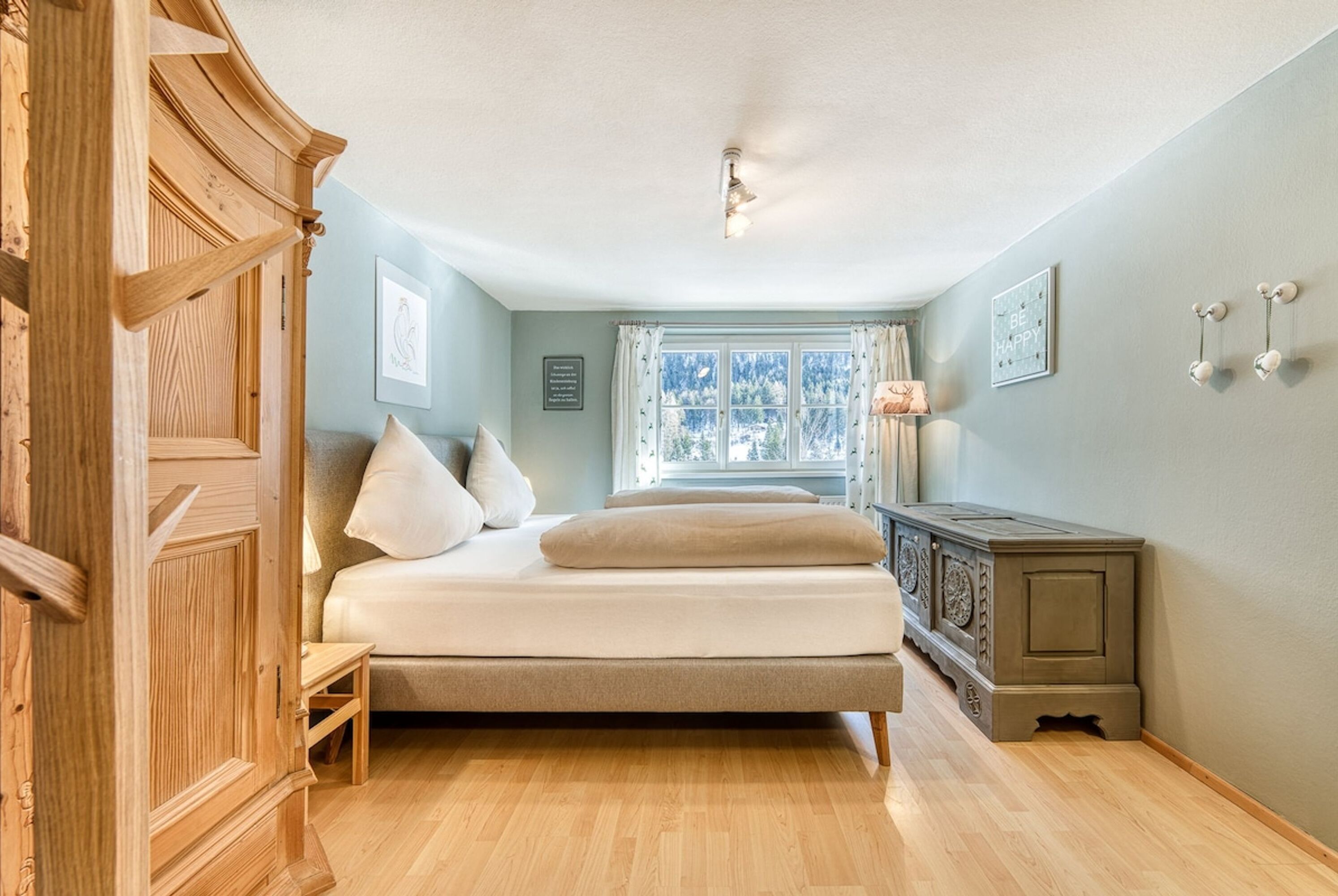 A bedroom with a bed, wooden wardrobe, and a window with curtains.