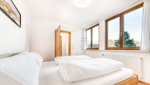 Un dormitorio con una cama de madera, ropa de cama blanca, una ventana con cortinas y una puerta que da a otra habitación.