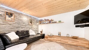 A modern living room with a leather sofa, a white round table, a fluffy rug, a wooden cabinet, and a mounted TV. - Ferienwohnung Zweisamkeit (Brand)
