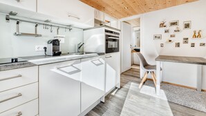 A modern kitchen with white cabinets, a wooden ceiling, and a dining area with a gray chair and table. - Ferienwohnung Zweisamkeit (Brand)