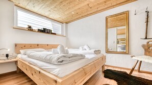 A wooden bed with white linens, a bedside table, a mirror, and a fur rug. - Ferienwohnung Zweisamkeit (Brand)