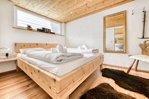 Un lit en bois avec du linge de lit blanc, une table de chevet, un miroir et un tapis en fourrure.