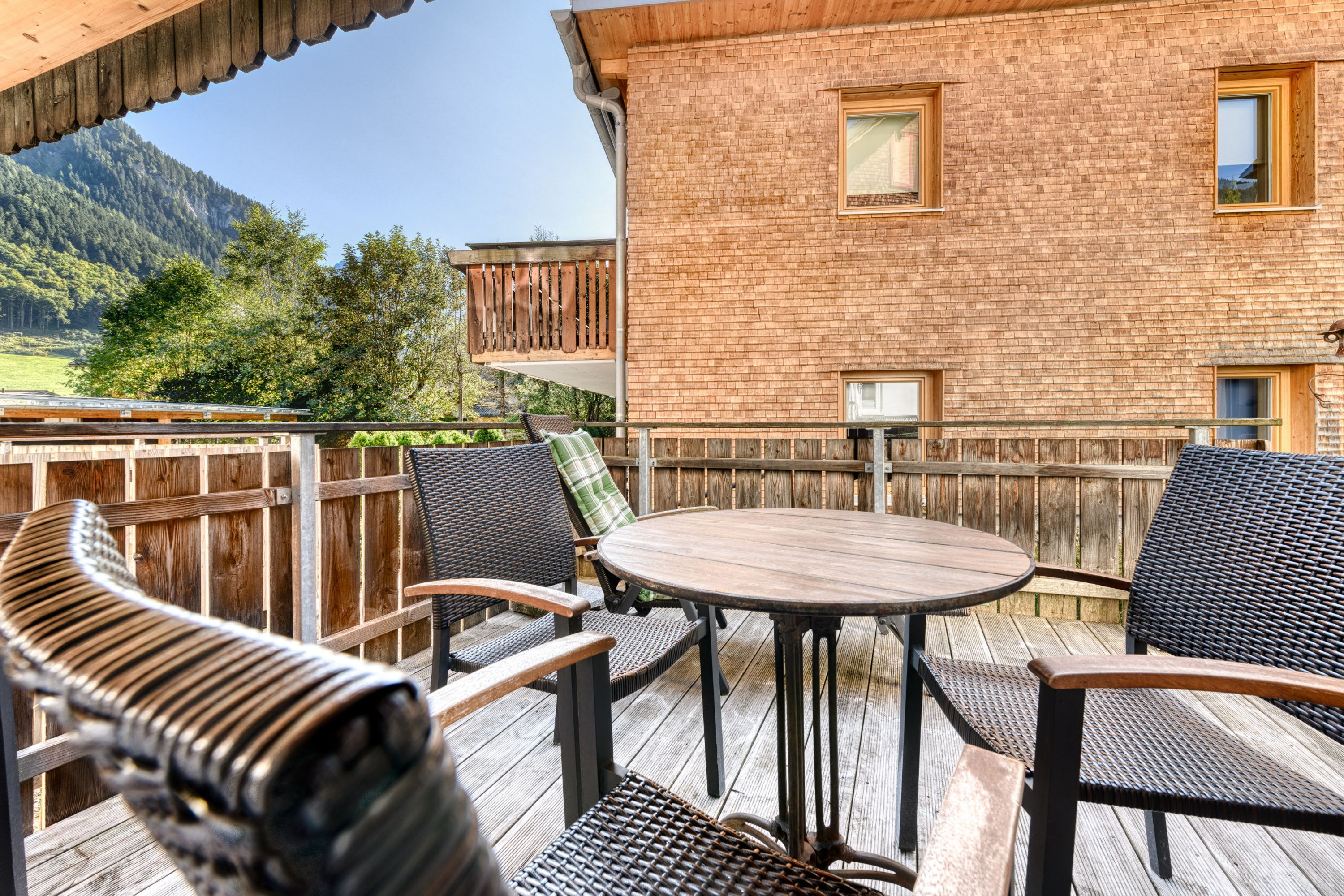 Eine Terrassengruppe mit Korbmöbeln und einem Holztisch, mit Blick auf eine Berglandschaft.