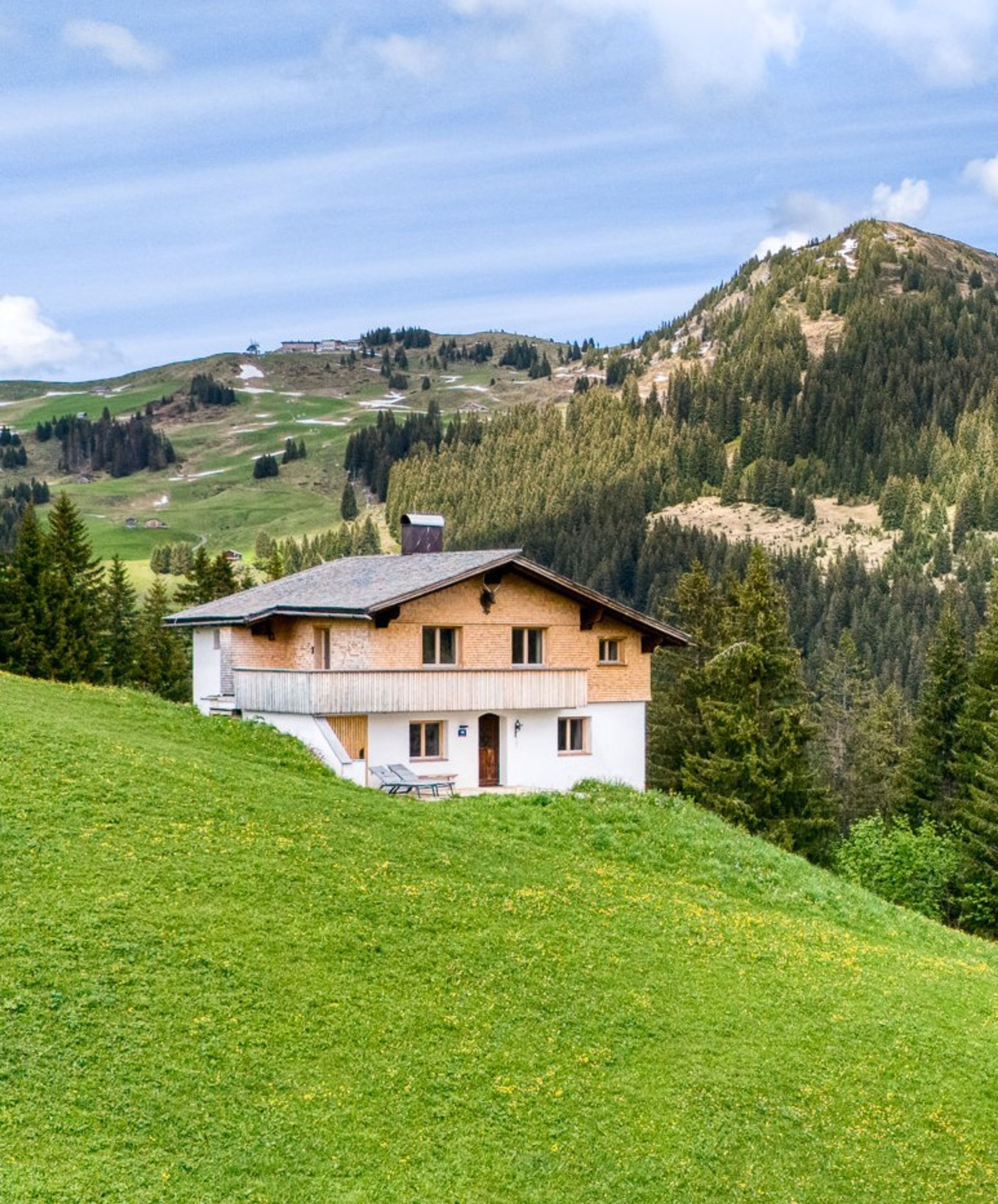 Een woonhuis met twee verdiepingen, een schuin dak, een balkon en uitzicht op een bergachtig landschap.