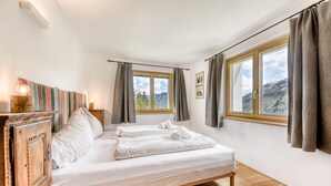 Un dormitorio con cama, un armario de madera, una ventana con cortinas y vistas a las montañas.