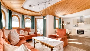 A spacious living room with a wooden ceiling, large windows with curtains, a dining area, and a kitchen. - Haus Alvier - 3-zimmer Fewo Rothorn mit Terrasse (Brand)