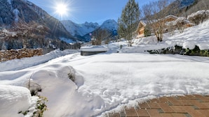 A snow-covered landscape with mountains, a wooden house, and a paved area. - Haus Alvier - 3-zimmer Fewo Rothorn mit Terrasse (Brand)