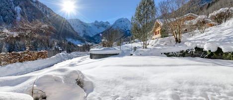 Ett snötäckt landskap med berg, ett trähus och en asfalterad yta.