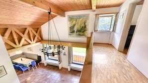 A spacious room with a high ceiling, wooden beams, a dining area with a table and chairs, and large windows offering a view of the outdoors. - Ferienhaus Haas in Vandans (Vandans)