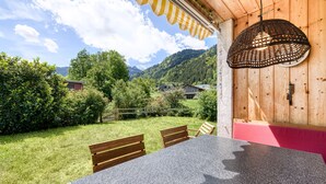 A dining area with a table and chairs, a hanging light fixture, and a view of a green landscape with trees and a mountain in the background. - Ferienhaus Haas in Vandans (Vandans)