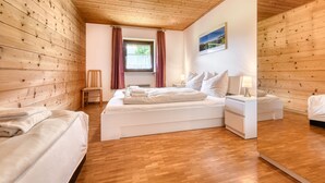 A room with wooden panel walls, a bed with white bedding, a nightstand with a lamp, and a window with curtains. - Ferienhaus Haas in Vandans (Vandans)