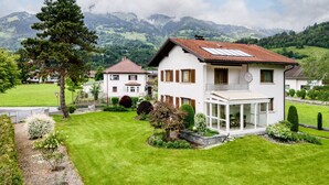 A two-story house with a balcony, surrounded by a well-maintained lawn and garden, with mountains in the background. - Landhaus Bergblick in Ludesch (Ludesch)