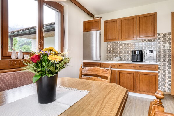 A kitchen with wooden cabinets, a stainless steel refrigerator, a coffee maker, and a window with a view of greenery. - Landhaus Bergblick in Ludesch (Ludesch)