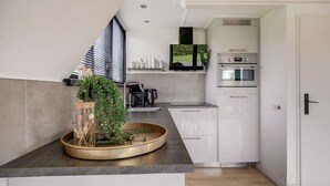 A modern kitchen with a built-in oven, a coffee machine, and a flat-screen TV mounted above the counter.