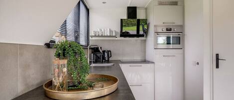 Een moderne keuken met een inbouwoven, een koffieapparaat en een flatscreen televisie boven de aanrecht.