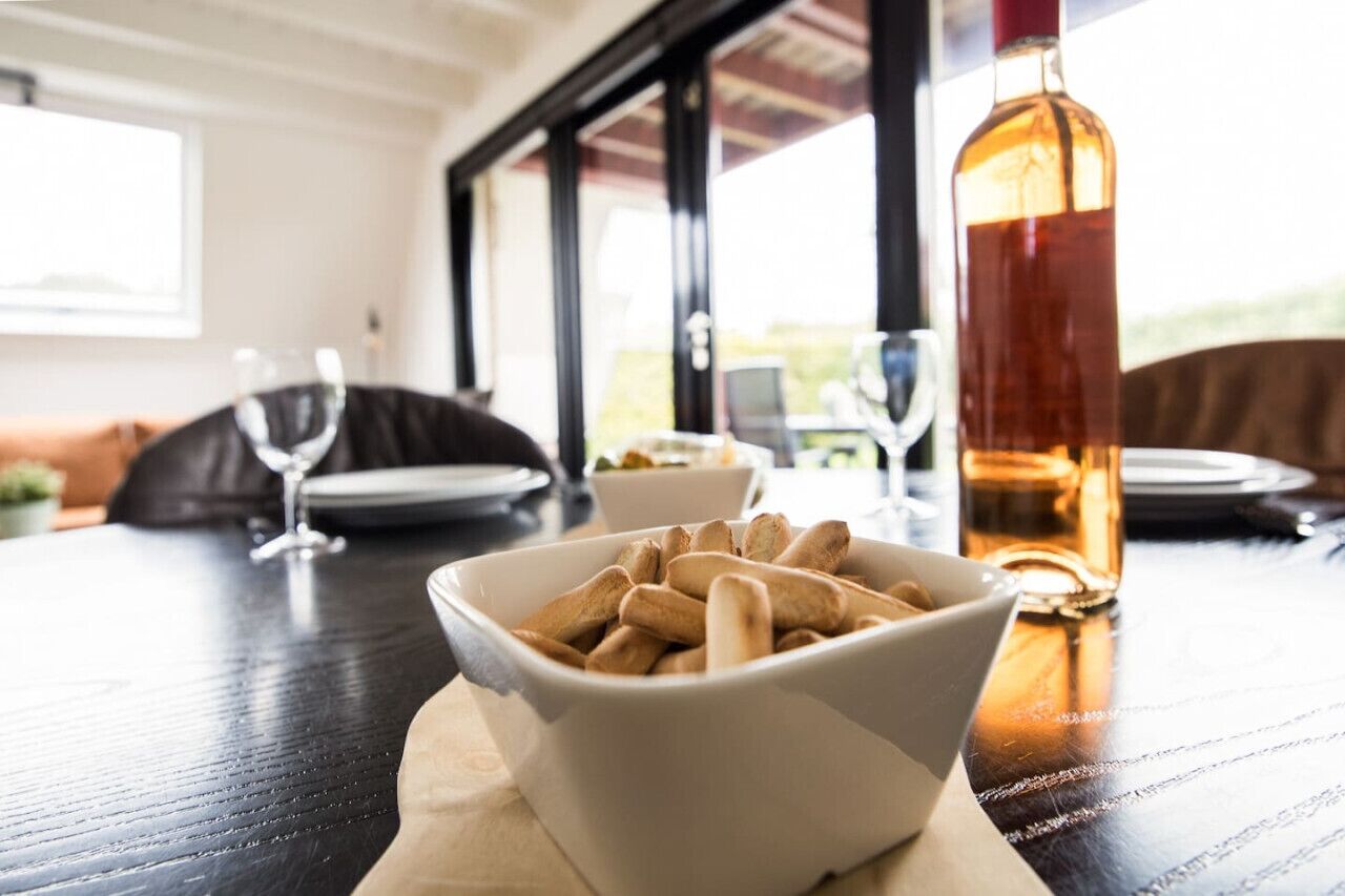 Una mesa de comedor con un cuenco de palitos de pan, una botella de vino y un ordenador portátil.
