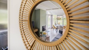 A room with a large mirror, a television, a dining area with a table and chairs, and a view of the outdoors. - Braamsluiper | Vakantiewoning met grote zonnige tuin (Zwiggelte)