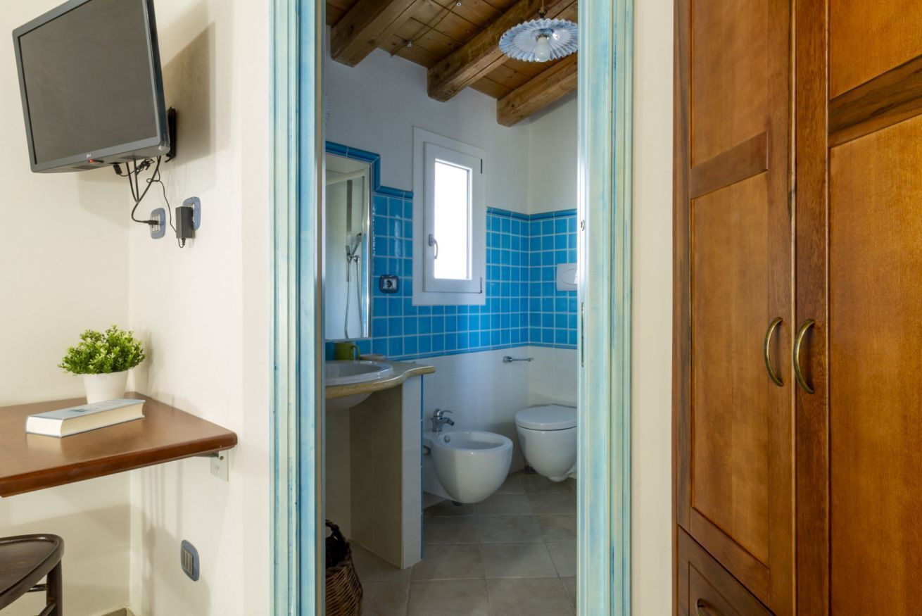 A bathroom with a blue-tiled wall, a wooden ceiling, a sink, a bidet, and a toilet.
