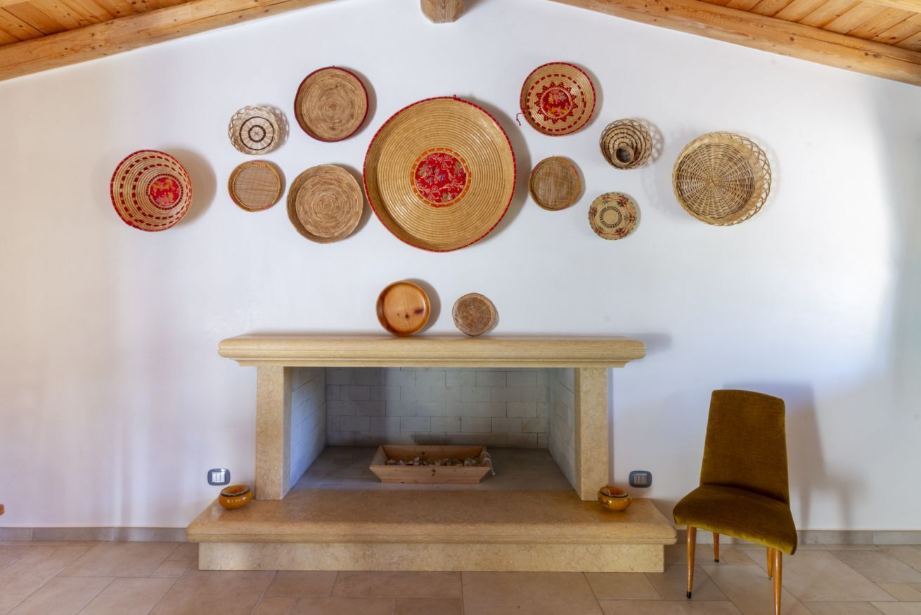 A fireplace with a mantel decorated with woven baskets, a wooden bench, and a modern chair.