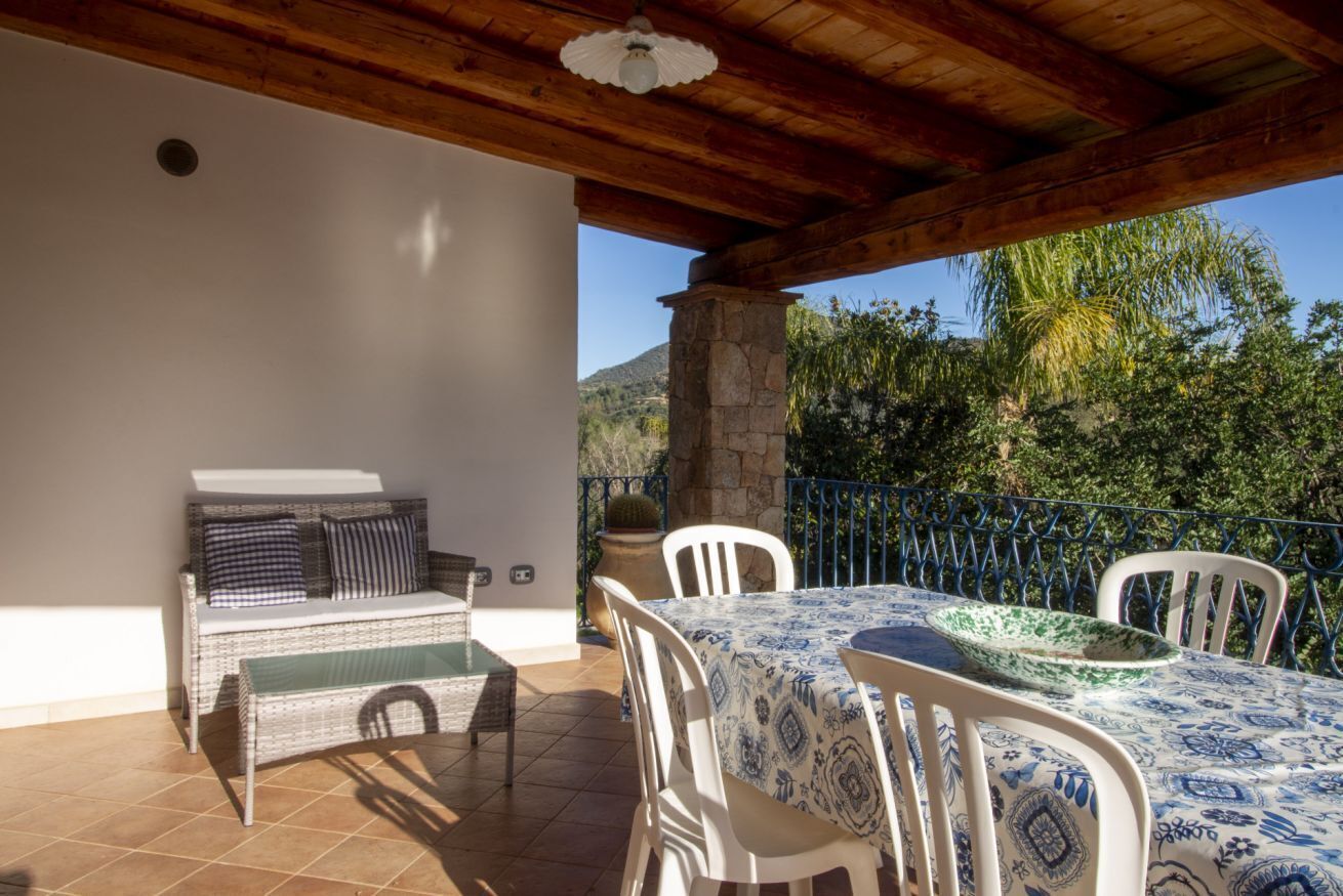 A patio with a table and chairs, a wicker sofa, and a stone pillar.