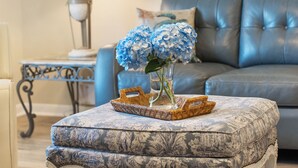 A living room with a blue sofa, a small side table, and a wicker tray with a vase of blue flowers. - PCB Beach Retreat with Pool and Private Balcony (Panama City Beach)