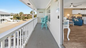 A balcony with a view of a parking area and buildings, a dining area with chairs and a table, and a living room with a sofa and a lamp. - PCB Beach Retreat with Pool and Private Balcony (Panama City Beach)