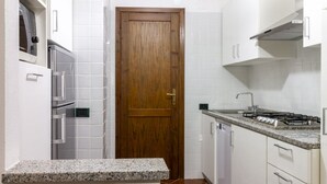 Une cuisine de taille réduite avec des meubles blancs, une porte en bois, un plan de travail en granit et une cuisinière à gaz.