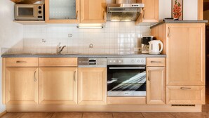 A modern kitchen with wooden cabinets, a built-in microwave, a stainless steel range hood, and a double oven. - Haus Alvier - 2-zimmer Fewo Zimba mit Balkon (Brand)