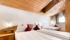 A bedroom with two beds, wooden headboards, and a sloped ceiling. - Haus Alvier - 2-zimmer Fewo Zimba mit Balkon (Brand)