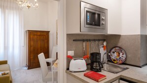 Una cucina moderna con forno a microonde, macchina da caffè e tostapane. C'è un'area pranzo con un tavolo e una sedia bianchi, e una porta in legno.