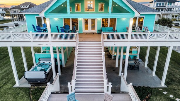 A turquoise two-story house with a covered deck, outdoor seating, and a staircase leading to the upper level.