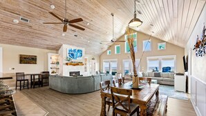 A spacious living area with a high ceiling, wooden flooring, and a dining table with chairs. There are sofas, a coffee table, and a fireplace.