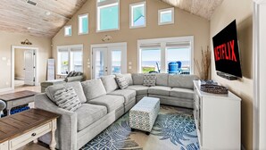 A spacious living room with a large sectional sofa, a wooden coffee table, and a flat-screen TV mounted on the wall.