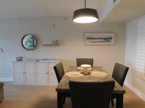 A dining area with a table, chairs, a pendant light, a cabinet, and artwork on the walls. - Santa Maria 2 bedroom, 2 bathroom, water view, walk to beach (Fort Myers Beach)