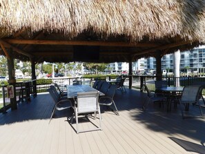 An outdoor patio with thatched roof, wooden deck, and metal-framed tables and chairs.