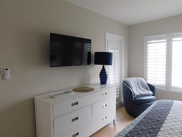 A bedroom with a bed, a chair, a dresser, a lamp, and a wall-mounted TV.