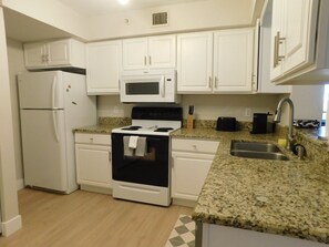 A kitchen with white cabinets, a white refrigerator, a stove, a microwave, a sink, and granite countertops.