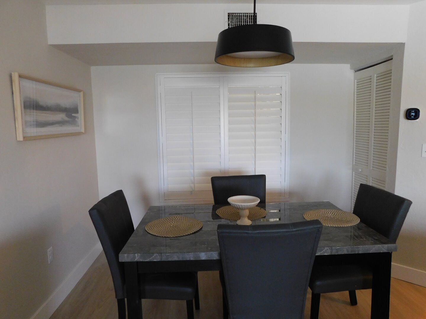 A dining area with a marble table, black chairs, a woven placemat, and a black pendant light.