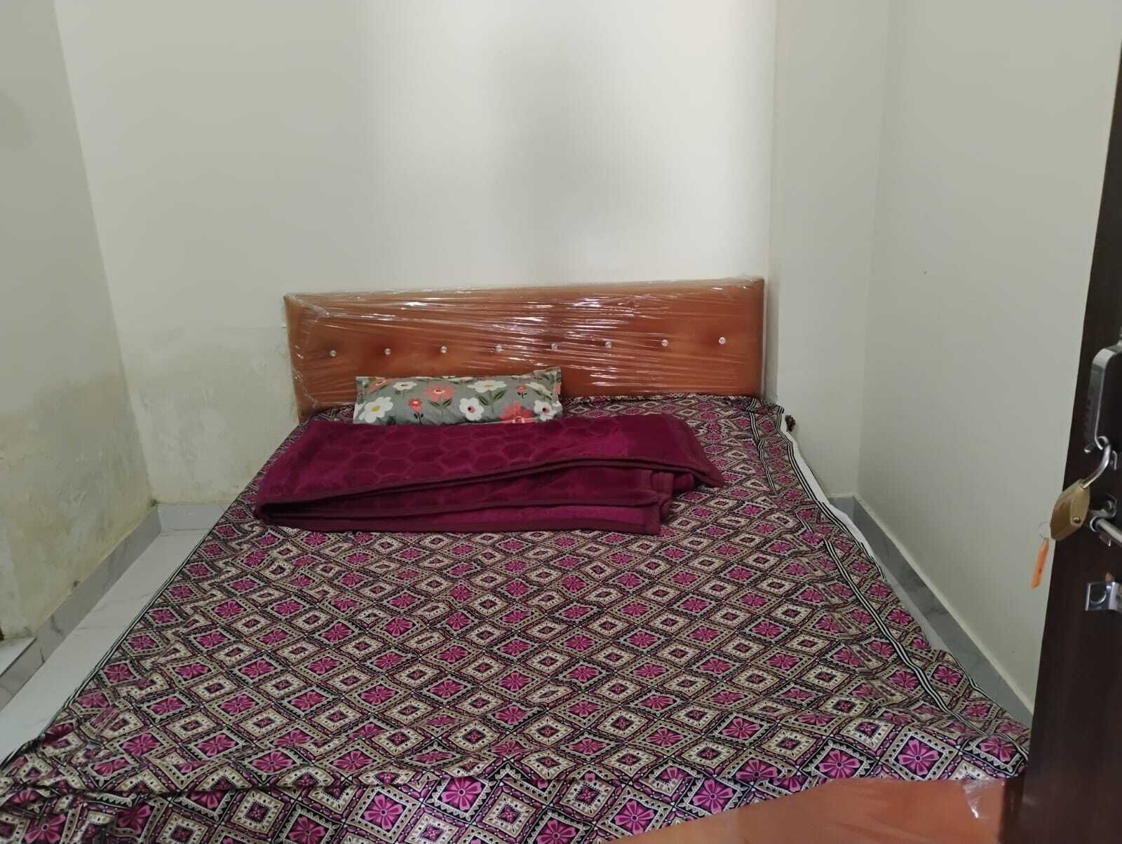 A small, single-bed room with a patterned bedspread, a wooden headboard, and a floral pillow.