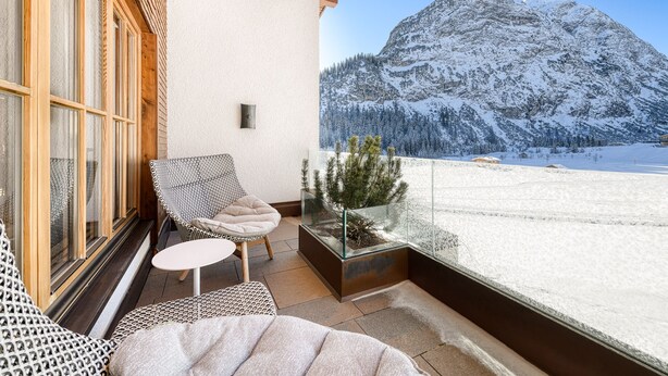 A balcony with a view of a snow-covered mountain, a glass-top table, and two patterned chairs. - Chalet Lilly-family Friends mit Ski In-ski out (Lech am Arlberg)