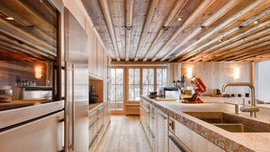 A modern kitchen with wooden beams, stainless steel appliances, and a large island with a sink. - Chalet Lilly-family Friends mit Ski In-ski out (Lech am Arlberg)