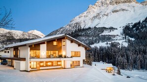 A modern two-story chalet with a large balcony, surrounded by snow-covered mountains and trees. - Chalet Lilly-family Friends mit Ski In-ski out (Lech am Arlberg)